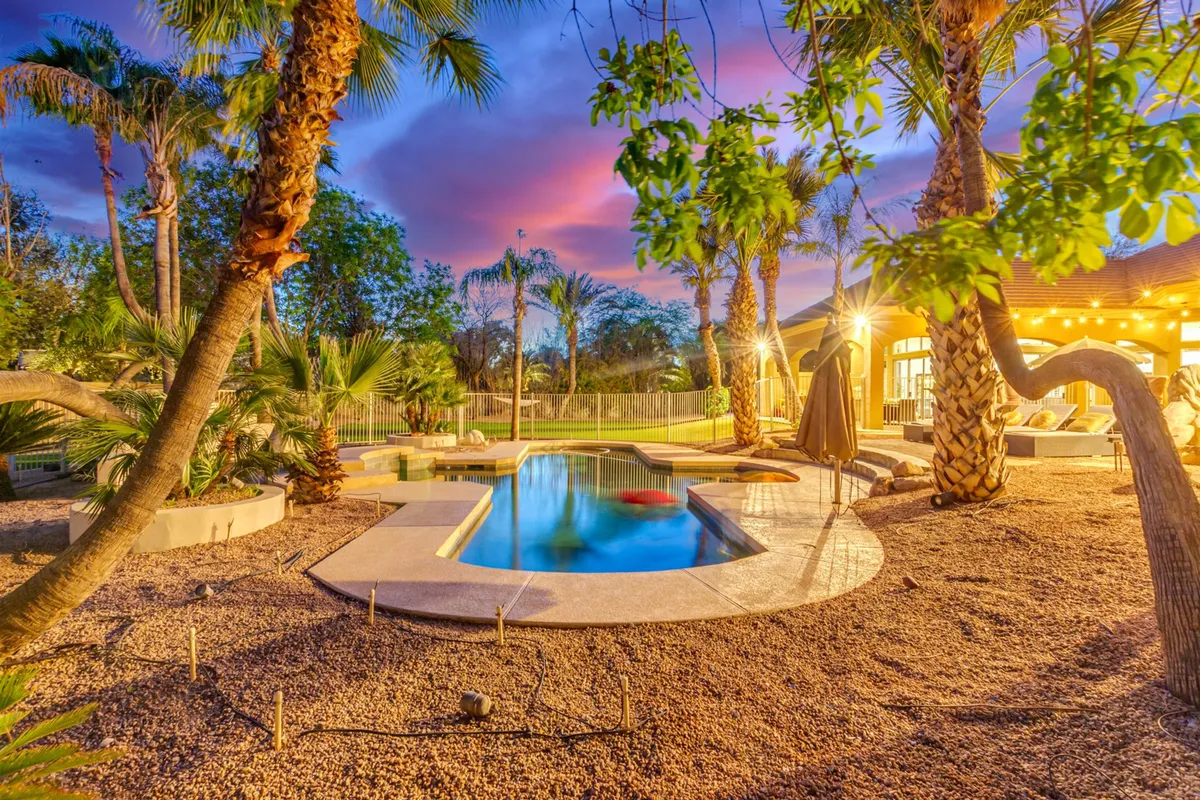 A tranquil exterior shot featuring a sparkling swimming pool, lush palm trees, a lounge area, and ambient landscape lighting. The setting is both festive and relaxing, ideal for outdoor dining, entertaining, or simply relaxing after a day out.