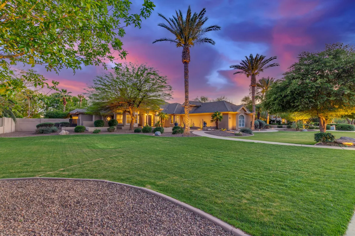 This exterior captures a lush green lawn with palm trees, a beautifully lit home in the background, and a vibrant sky at dusk. The scene is serene and inviting, perfect for evening gatherings or simply enjoying the Arizona sunset after an active day.
