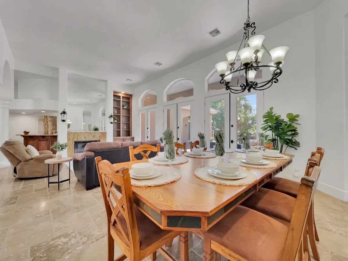 A warm, inviting dining area is at the heart of this interior, with a large dining table set for a meal, surrounded by plush seating and illuminated by a stylish chandelier. The space seamlessly opens into a living area with soft, inviting seating, reinforcing the idea of interconnected spaces ideal for celebrations and family moments.