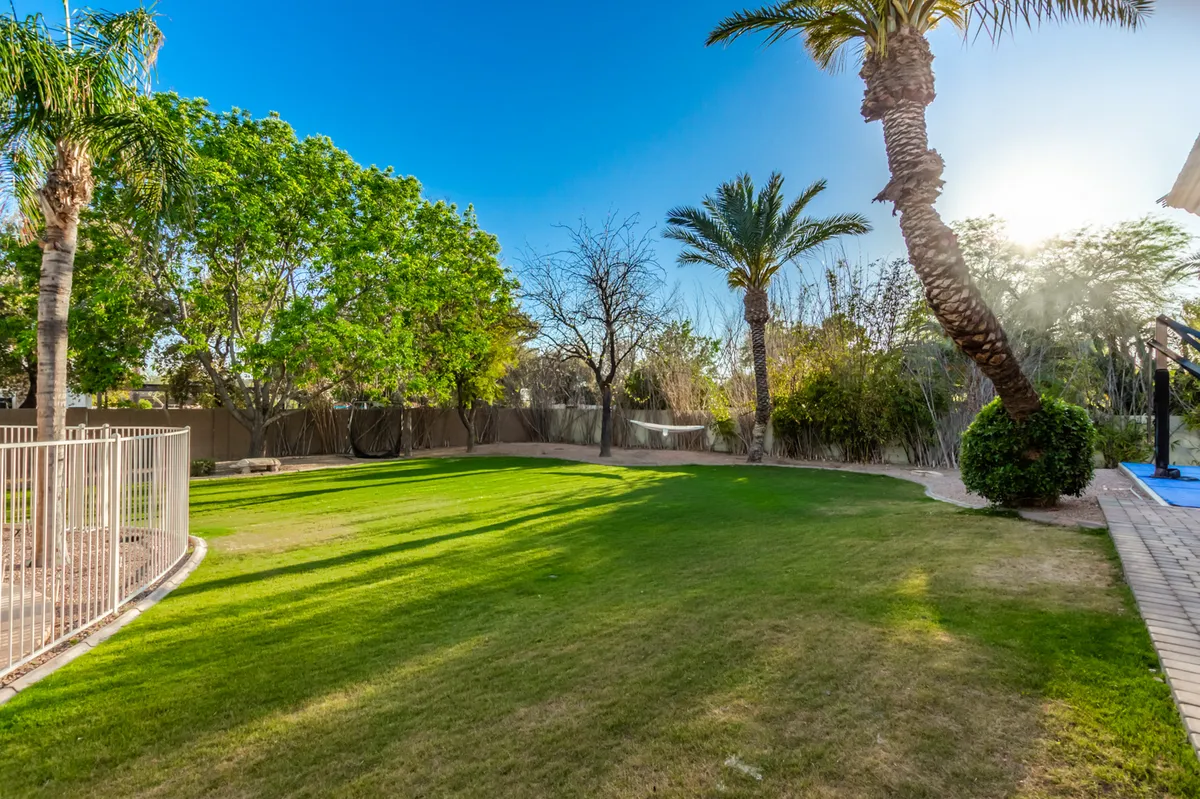 A vibrant, grassy lawn stretches out, framed by palm trees and decorative fencing, offering plenty of space for children to play, family picnics, or simply soaking up the sun in tranquil privacy.