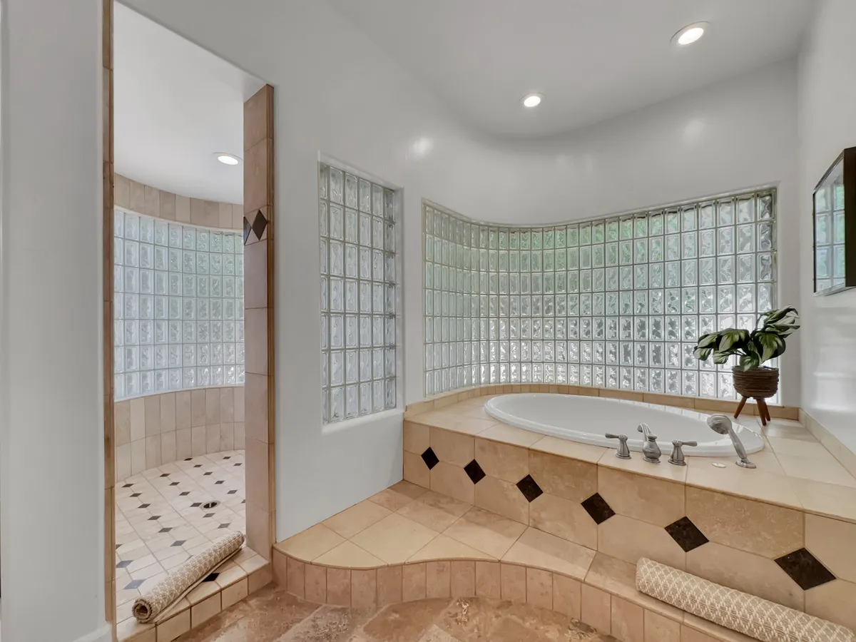 A spa-inspired bathroom with a corner jacuzzi tub, glass block walls for privacy and natural light, textured tiles, and a leafy potted plant. The space exudes tranquility and luxury, perfect for indulgent self-care routines.