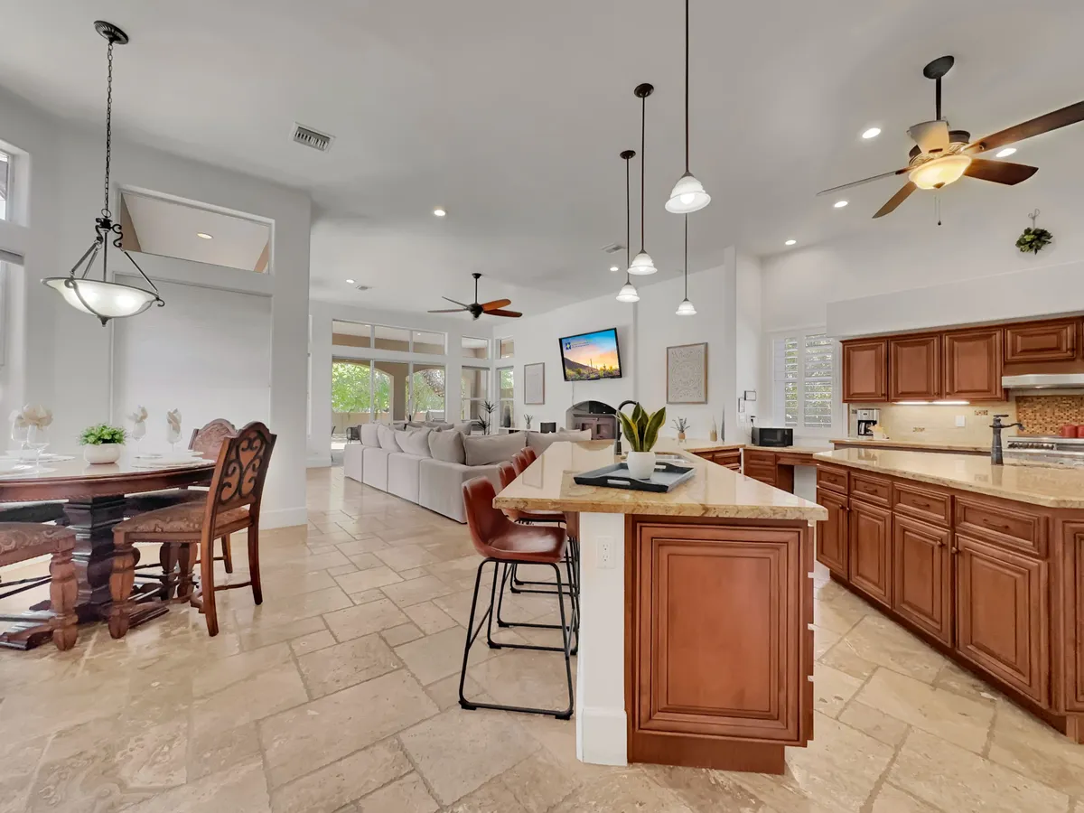 This image showcases an inviting, open-concept interior with a kitchen island and bar stools, a spacious dining table, and a comfortable living area with a sofa. The seamless flow between the kitchen, dining, and family room illustrates the heart of the home where cooking, dining, and relaxing all happen together. Natural light fills the space, enhancing the warmth and togetherness.