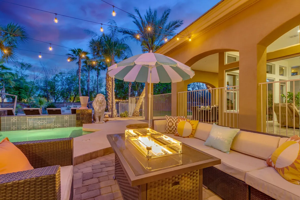 This exterior image features a cozy fire pit area surrounded by lounge seating and umbrellas, with palm trees and string lighting enhancing the ambiance. The inviting setup is ideal for evening gatherings, outdoor celebrations, and relaxed conversations under the stars.