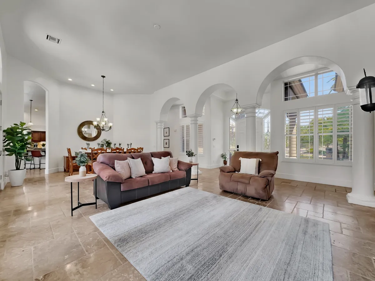 An inviting interior space with a sofa, coffee table set for gathering, a dining area in the background, and soft arches and windows letting in natural light. The layout is open and sociable, supporting both casual and festive gatherings.