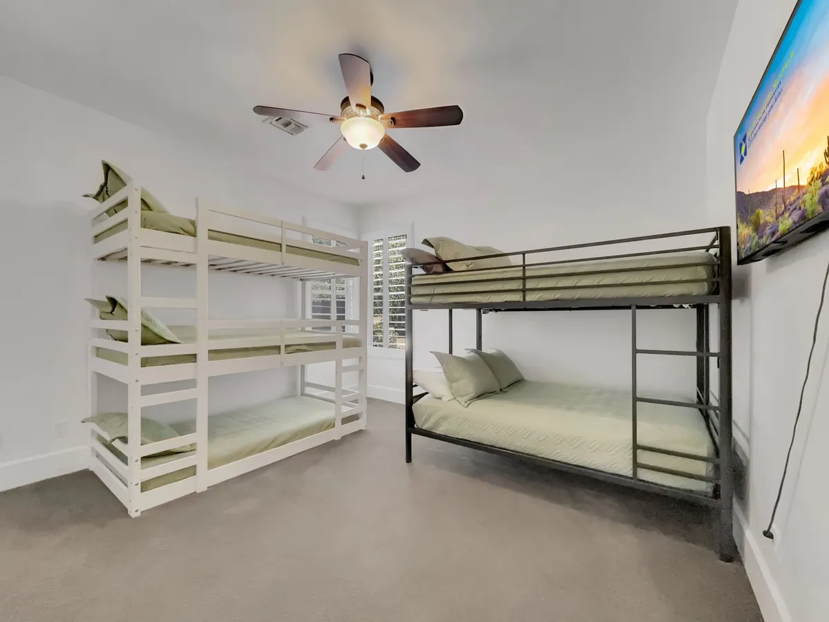 A cheerful and comfortable bunk room with sturdy bunk beds, a ceiling fan for comfort, and a TV for entertainment. The space is clearly designed to be both fun and functional for children, with inviting, playful touches.