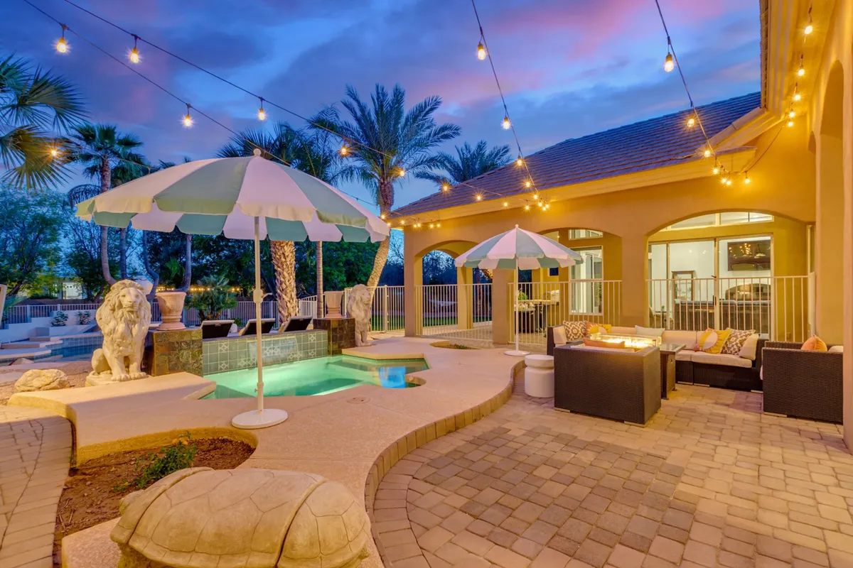 This exterior image showcases a sparkling swimming pool surrounded by an outdoor seating area, decorative lion statues, and warm string lights. The setting feels festive and welcoming, suggesting lively gatherings and poolside fun as the sun sets.