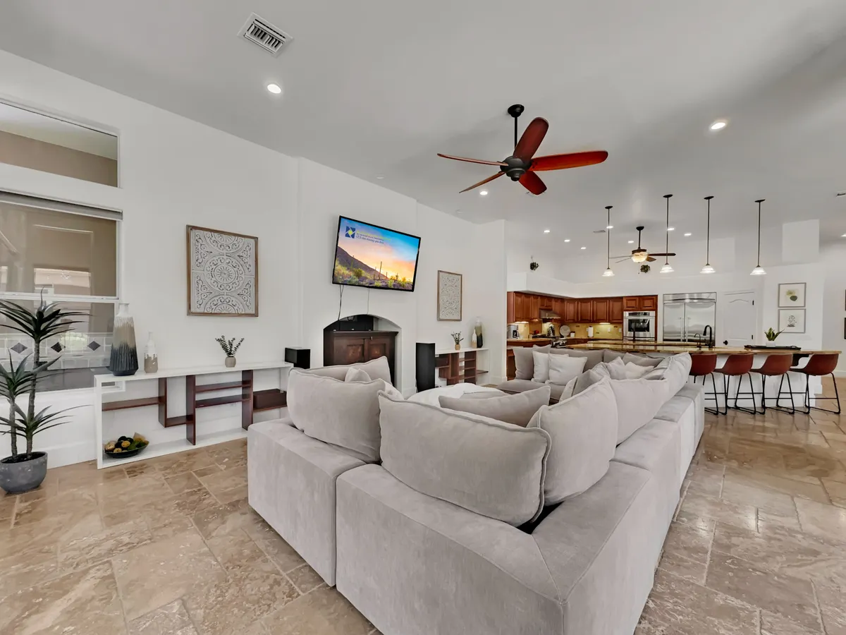 A contemporary open-plan space featuring a spacious sectional sofa facing a large flat-screen TV, with the kitchen area visible in the background. Decorative elements and natural light create an atmosphere that’s both stylish and comfortable—perfect for movie marathons and family hangouts.