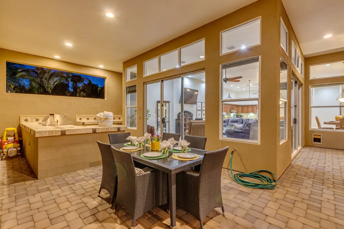 An inviting alfresco dining area with a beautifully set table, outdoor kitchen, and large windows showcasing the home's interior. The setting is ideal for entertaining guests, summer barbecues, and intimate gatherings under the stars.