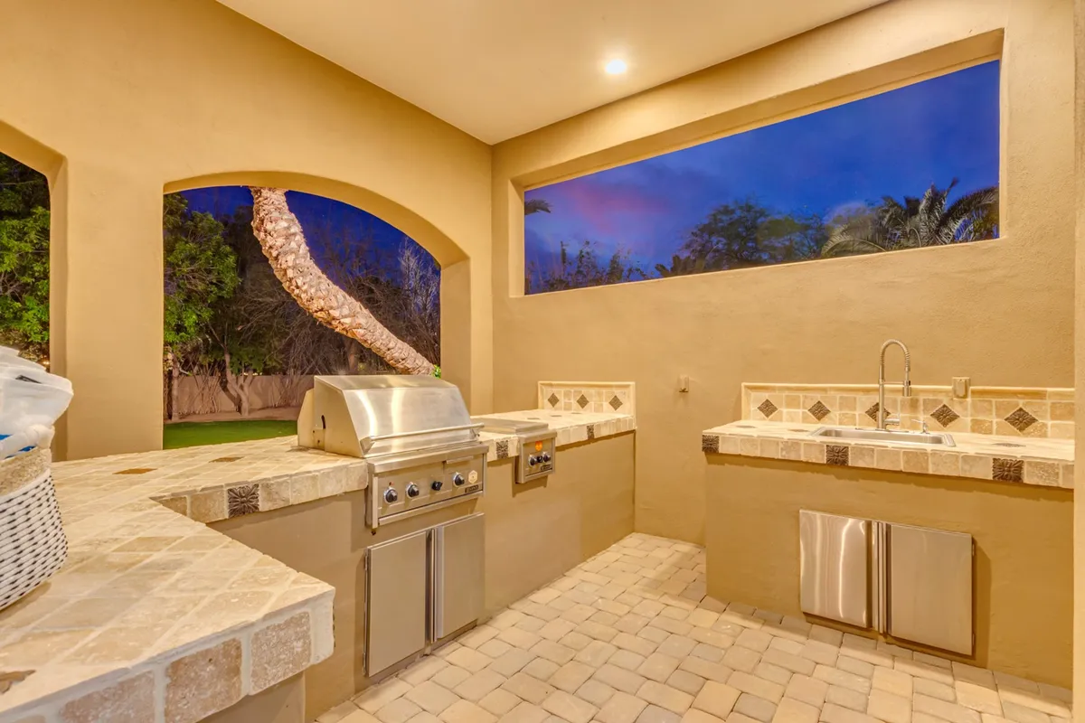 This image showcases an outdoor kitchen grill with a countertop, set against a window view. The scene is relaxed and designed for barbecuing and entertaining guests outdoors, evoking a sense of celebration and camaraderie after a day out.